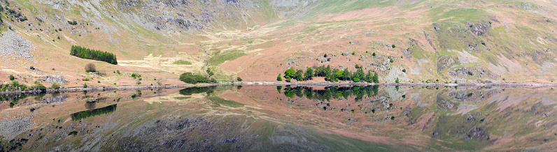 Panoramic photo of Haweswater reservoir on a still early summer day, with mirror-like reflections of the mountain sides and trees on the surface of the water, in the English Lake District