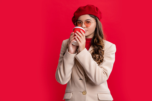 young stylish teen girl drinking coffee. photo of stylish teen girl with brunette hair. stylish teen girl isolated on red background. stylish teen girl in studio.