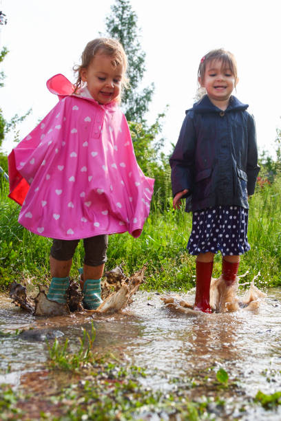 Two little girls jumping in mud puddles stock photo