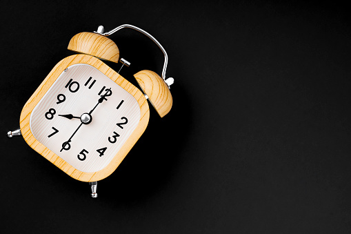 Vintage wooden alarm clock on black background with copy space.