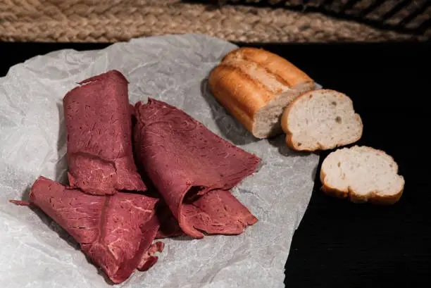 Photo of cold cut platter, deli meat and french baguette as luncheon snack on cooking paper dark background