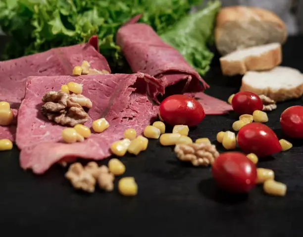 Photo of Deli meat cold cut  with vegetables, cherrry tomatoes, sweet corn, walnuts and lettuce salad leaves, french baguette