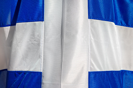 Greece flag fabric background . Greek flag waving . White cross at blue