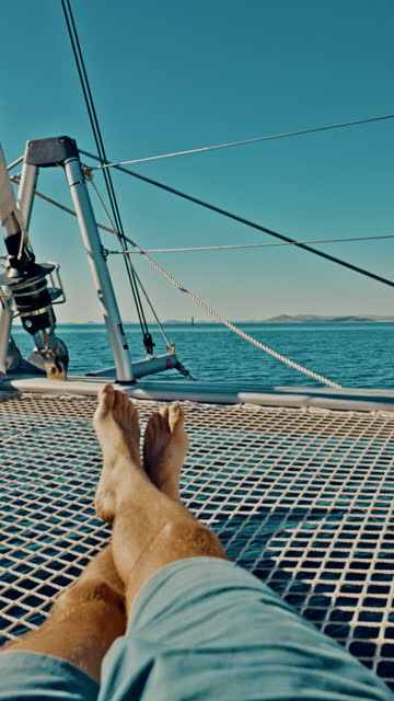 WS Unrecognizable man lying on a trampoline of a catamaran sailing the sea