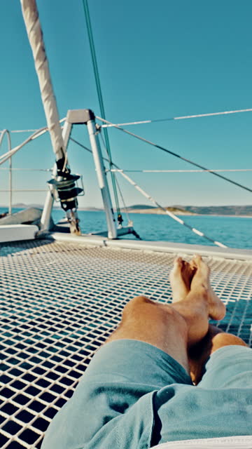 POV Unrecognizable man have a cup of tea while he lying on a trampoline of a catamaran