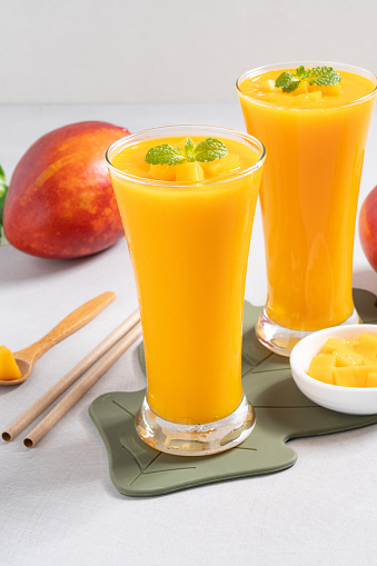 Fresh beautiful delicious mango juice. Close up design concept of smoothie cold drink in glass cup with glass straw on gray table background.