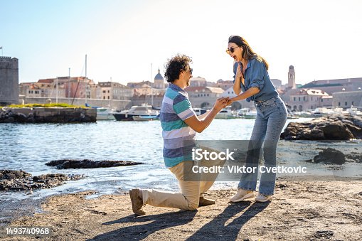 istock Man proposing to his girlfriend by the sea edge on a beautiful sunny day 1493740968