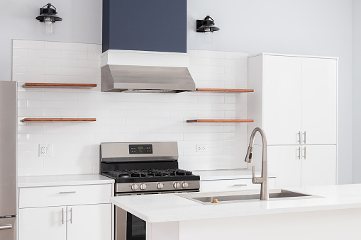A kitchen detail with white cabinets, floating wood shelves on a white subway tile backsplash, and mounted lights around the blue oven hood.