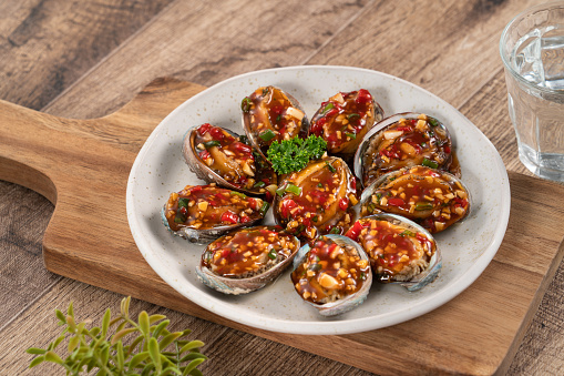 Delicious steamed abalone with spicy tomato sauce, Taiwanese five flavor sauce on wooden table background.