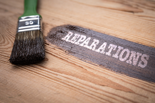 Reparations Concept. Green brush and painted wooden board with text.
