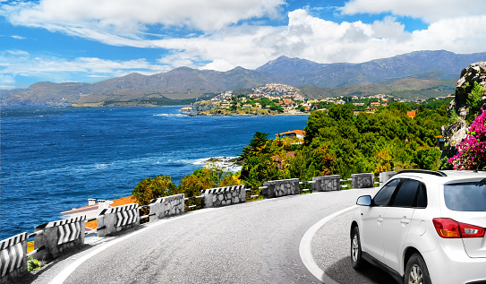 A white car drives by the road in mountains to the sea. Car trip and summer vacations background. Colorful seascape in the Mediterranean.