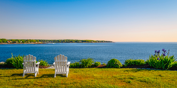 Two white wooden benches on the beach. Cape Cod Adirondack Chair on the green hill. Tranquil relaxing seascape over Short Sands Beach in Cape Reddick, York, Maine