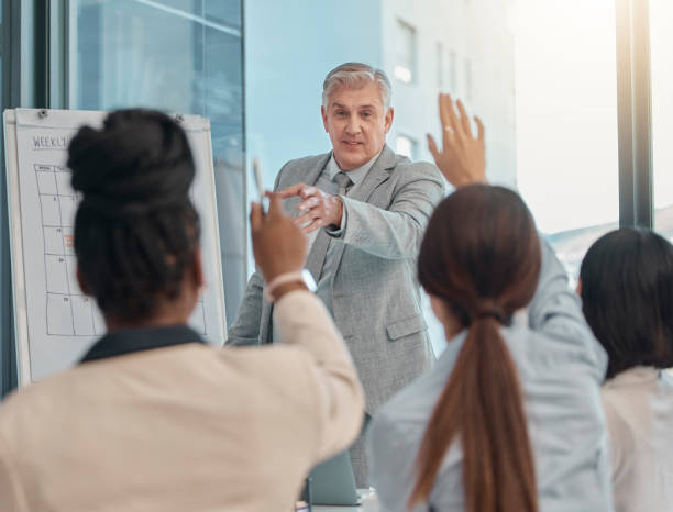istock Senior businessman, coaching and presentation with question in team collaboration or engagement at office. Elderly male CEO leader or coach training staff with hands raised in FAQ, teamwork or answer 1493763632