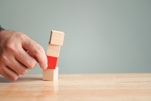 Hand picking red wooden cube blocks poses a risk of collapse of the entire structure. Risk management and decision making concept. Dangerous and choice theme.