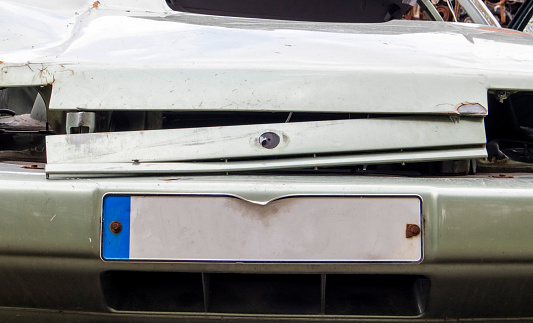 The front of the car with damage to the bumper after the accident. Empty license plate. Close-up of the surface of the license plate in front of the car, square license plate of the car