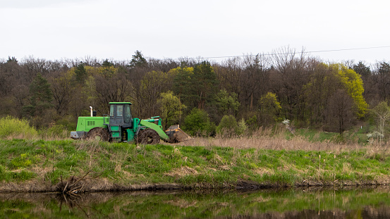 The tractor rides along the bank of a river or lake in the forest