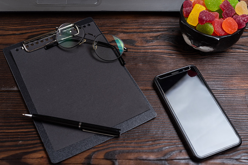 Tablet and pen. Glasses and a pen lying on a notebook. Smartphone and laptop beech on the table. Black notepad on the work table. View from above.