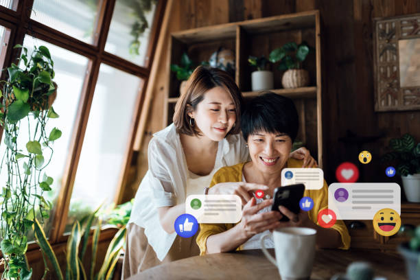 Happy Asian senior mother and daughter using smartphone together joyfully at home. Checking social media on mobile phone, receives notification, likes, views and comments. Social media. Multi-generation family and technology. People network and technology. feliz madre e hija mayores asiáticas usando el teléfono inteligente juntas alegremente en casa. revisando las redes sociales en el teléfono móvil, recibe notificaciones, me gusta, vistas y comentarios. redes sociales. familia multigeneración y tecnolo
