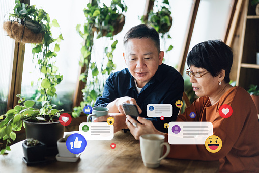 Asian senior couple relaxing at home and using smartphone together. They are learning and checking social media, receives notification, likes, view and comments. Senior couple lifestyle using technology, social media and digital online, silver surfers