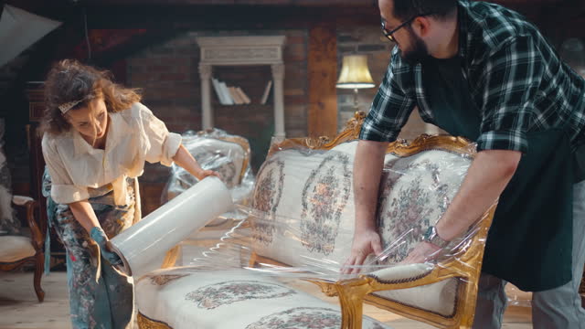 Antique shop owners wrapping with a foil old antique sofa for shipping