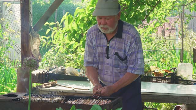 an elderly man with a beard cooks meat steaks on the grill