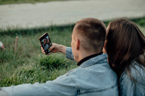 young fashionable couple smiles while looking at the phone in the park, selfie