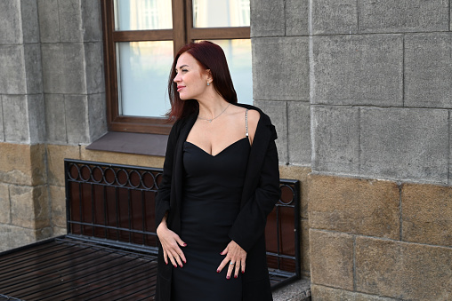 a confia confident young attractive woman in a black dress and high-heeled shoes walks through the streets of the city, the woman smiles and enjoys lifedent young attractive woman in a black dress and high-heeled shoes walks through the streets of the city, the woman smiles and enjoys life