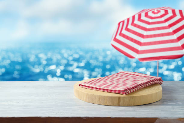 istock Summer mock up for design and product display presentation. Empty wooden podium with tablecloth on table over blurred sea beach background 1493789355