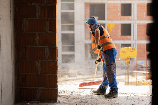 Unrecognizable mid-adult construction worker, using broom, to clean the dust on the construction site