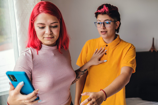 lesbian couple having heated argument while looking at cell phone. Tension is reflected in their faces and gestures, evidencing moment of conflict in their relationship.