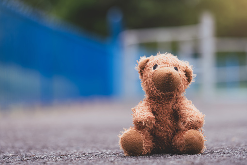 Lost teddy bear toy sitting  on playground floor in gloomy day,Lonely and sad brown bear doll sitting alone in the park, Lost toy or Loneliness concept,International missing Children day