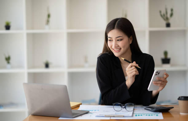 istock Young smart Asian businesswoman working at the working table and using her smartphone at the same time. 1493799536