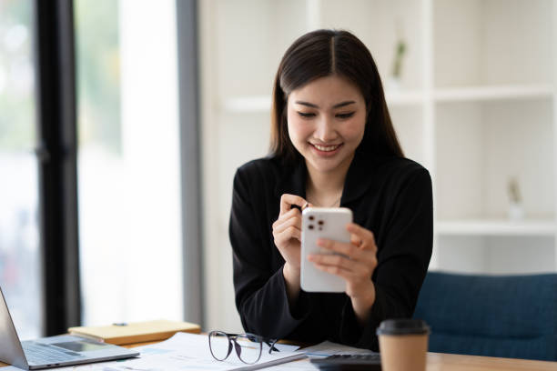 istock Young smart Asian businesswoman working at the working table and using her smartphone at the same time. 1493801364