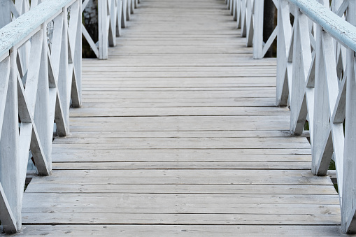 Aged wooden bridge with railings criss-cross close-up, handmade painted with white paint, leading into distance. Blurred perspective. Metaphor of life path, lack of visibility of destination point.