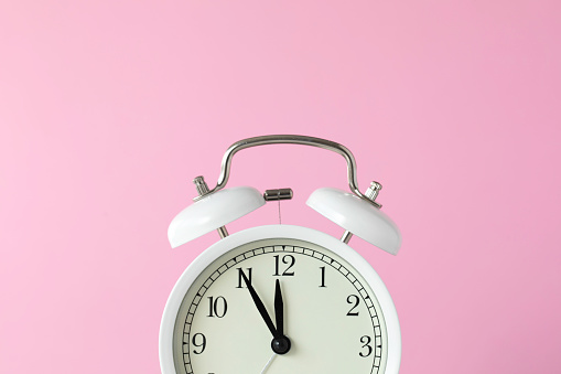Retro style alarm clock on pink background.