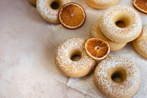 Orange flavored baked doughnuts dusted with powdered sugar; mini homemade fruit bagels on light background
