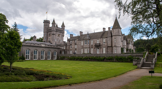 Royal Balmoral Castle in Scotland in summer with clouds and park with mowed lawn. Stone steps and a path through the park.