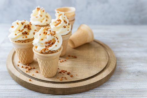 Cone cakes with butter cheese frosting and caramelized nuts on wooden board; kids party food; creamy crunchy dessert ice cream alternative
