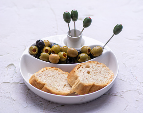 Fresh, Green and black olives served with bread in a white ceramic plate