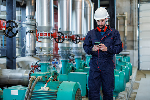 A young man in a heating plant uses his phone to write SMS messages during a brief pause from his responsibilities