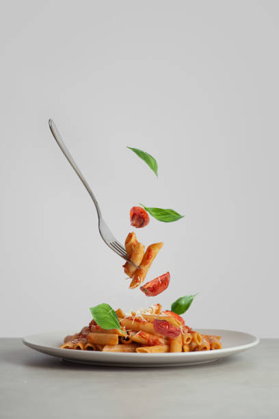 Pasta on a fork with tomatoes and basil falling into a plate. levitating food