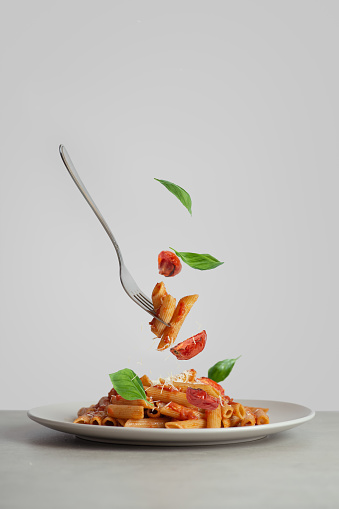 Pasta on a fork with tomatoes and basil falling into a plate. levitating food