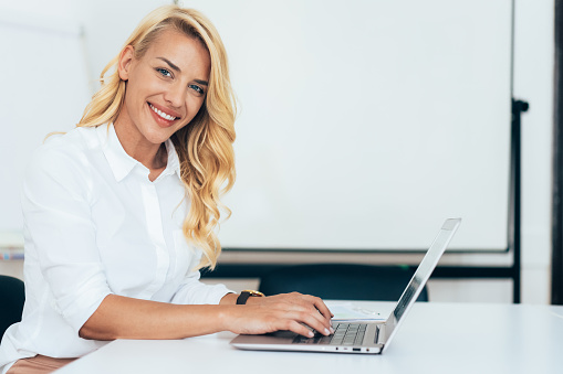 Portrait of beautiful Businesswoman using laptop at desk. Confident female professional is working at office, looking at camera and smiling.
