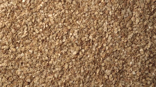 Oatmeal or crunchies form a slowly rotating textured background. Concept of healthy food - cereal breakfast. Close up, top view. Copy space for advertising text.