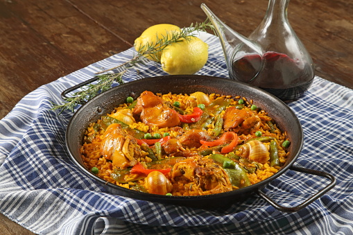 Valencian paella with porron of red wine on the wooden table