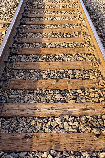 Railroad tracks in warm light showing cold steel rails. Low sun angle warms the gravel and railroad ties, while cool blue light illuminates the steel rails. A background or detail abstract image.