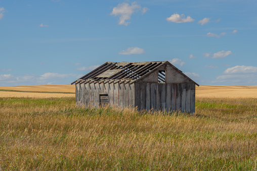 Old abandoned farm building in the prairie with a cloudy blue sky, Alberta, Canada