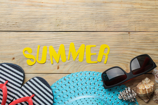 The word summer made of paper yellow letters and summer, beach accessories on a natural wooden background. summer. vacation. relaxation. top view