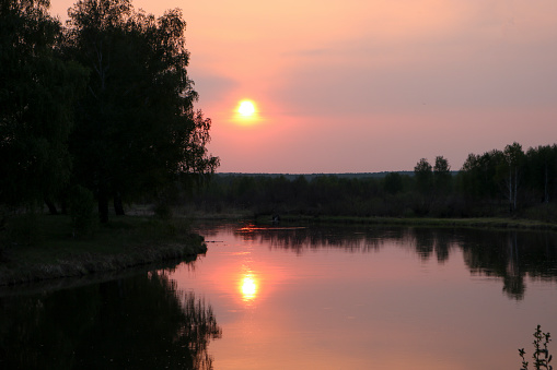 A colorful sunset over a calm river among birch groves. Summer evening.