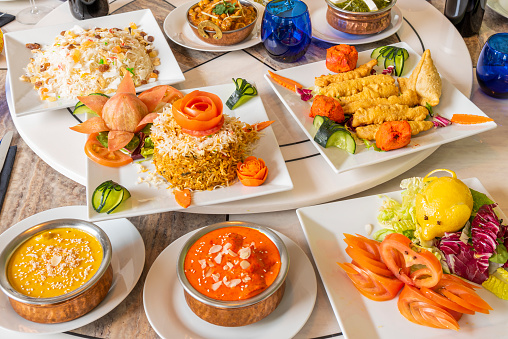 Set of Indian food dishes with basmati and kashmir rice, red curry, onion bhaji, palak paneer, korma, tomato and lettuce